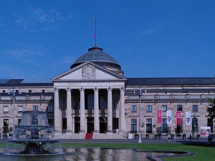 Wiesbaden - hessisches Staatstheater Historisches Gebäude mit Säulen und Statue, umgeben von Grünanlagen und klarem Himmel.