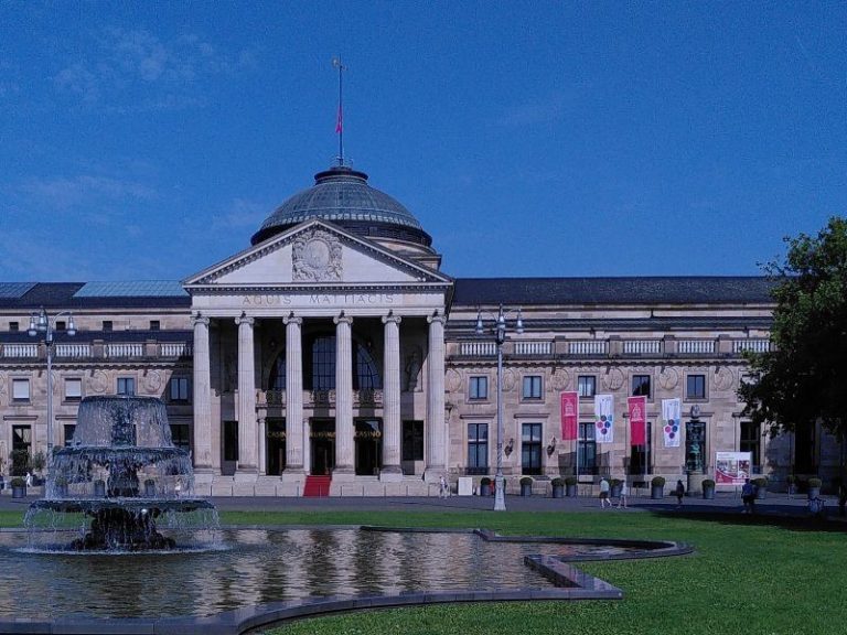 Wiesbaden Entdeckungstour - Kurhaus und Bowling Green Historisches Gebäude mit Säulen und Kuppel, umgeben von einem Garten mit Brunnen.