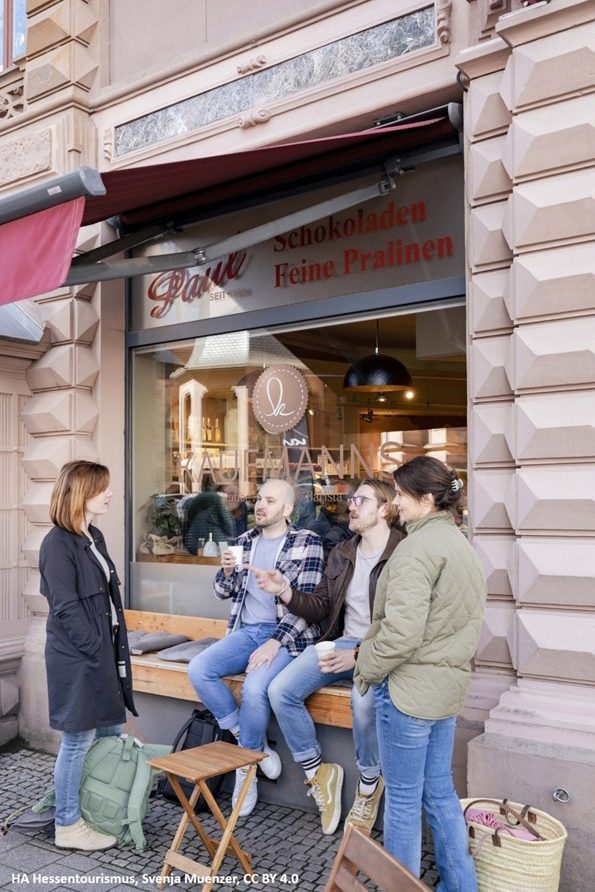 Digitale Zeitreise - Eine Gruppe bei der Pause am Café Kaufmanns Eine Gruppe sitzt vor einem Café und unterhält sich.