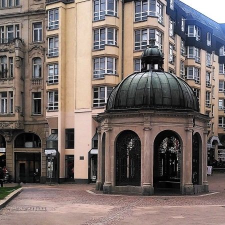 Wiesbaden Sightseeing Kochbrunnen Historischer Pavillon mit Kuppel in einem urbanen Platz zwischen Gebäuden.