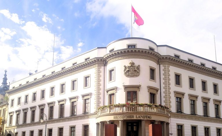 Wiesbaden Sightseeing Highlights Stadtschloss Ein klassizistisches Gebäude in schlichtem weiß und grau mit wehender Fahne.