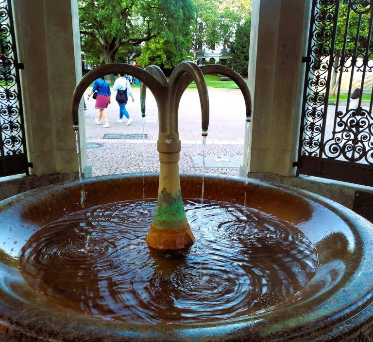Wiesbaden in einem Tag erkunden Thermalquellen Brunnen mit Wasserlauf, umgeben von einer grünen Parklandschaft.