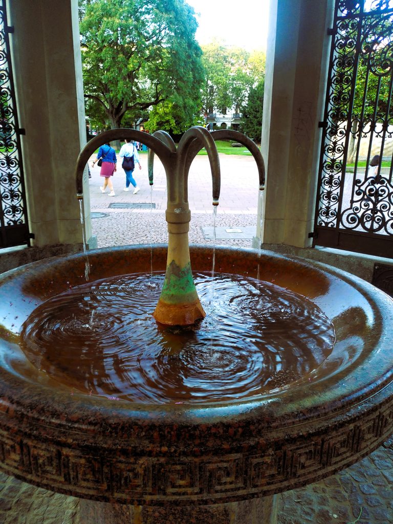 Digitale Zeitreise - Kochbrunnenspringer Brunnen mit Wasserfontäne und verzierter Steinfassung.