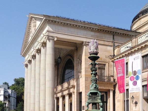Wiesbaden Highlights - Kurhaus Foyer Klassizistisches Gebäude mit Säulen und dekorativem Laternenmast vor blauem Himmel.
